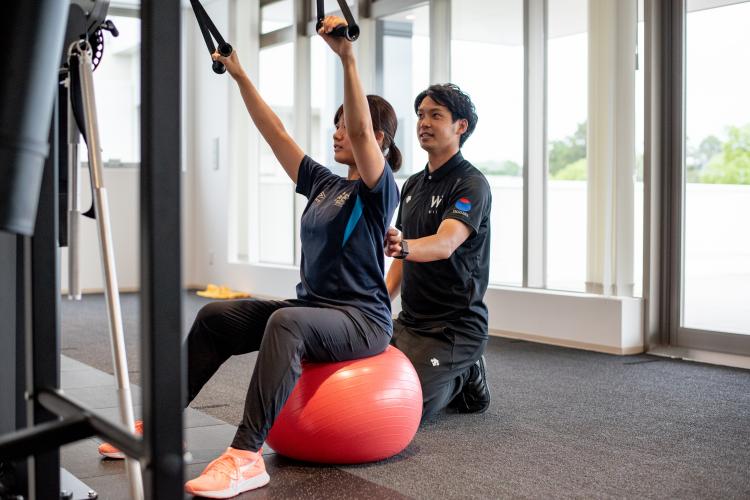 ラットプルダウンをしているクライアントと指導するアスレティックトレーナー